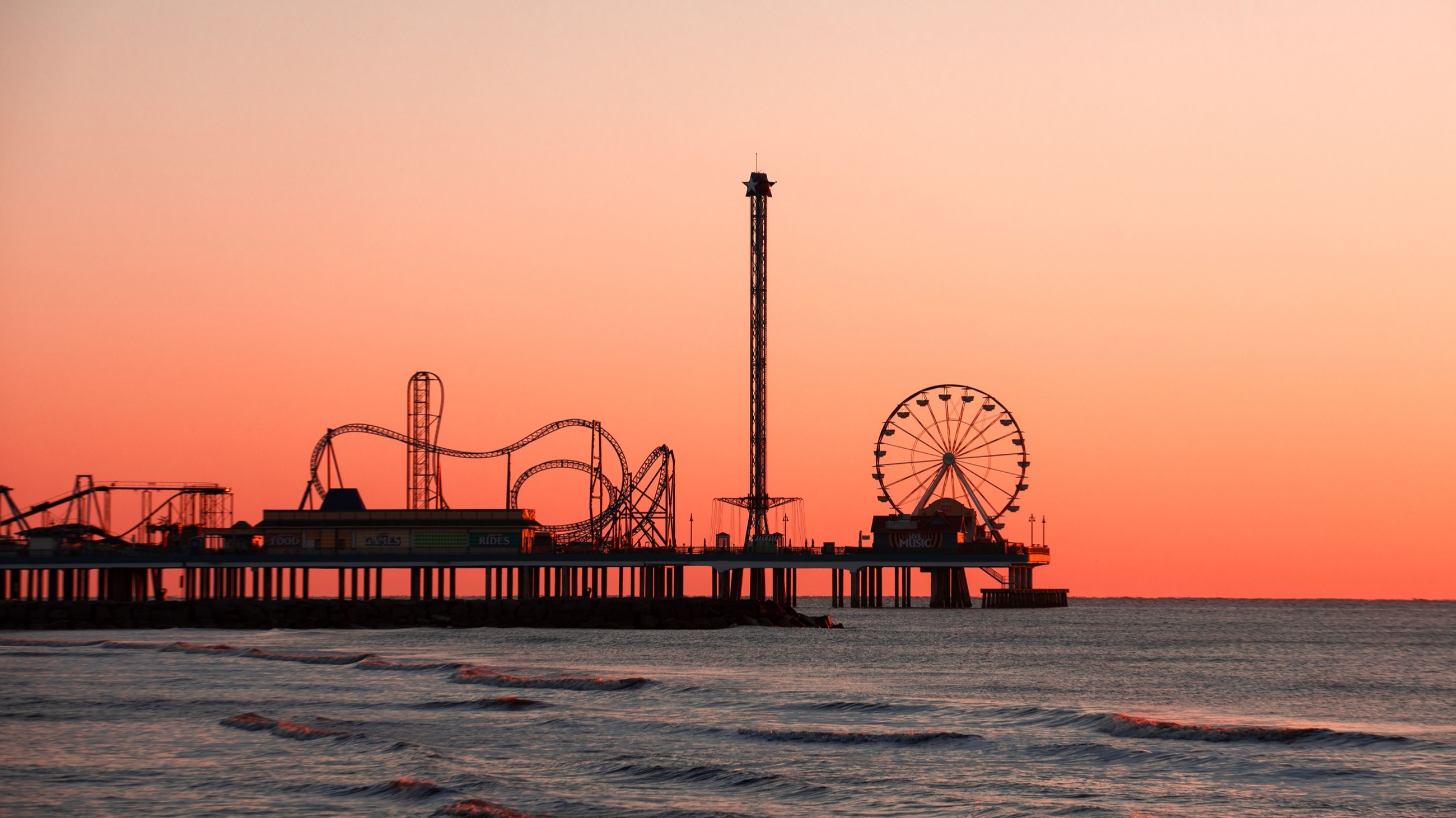 Silueta de un parque de diversiones sobre un muelle al atardecer